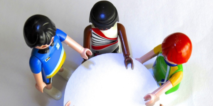 Figurer av plats står vid ett runt bord. Symboliserar samverkan skola arbetsliv