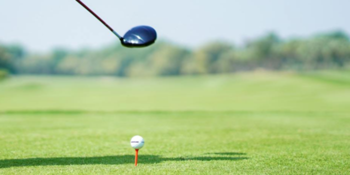 Uppeggad golfboll på golfbanan. Ovanför syns en golfklubba på väg att slå på bollen. 