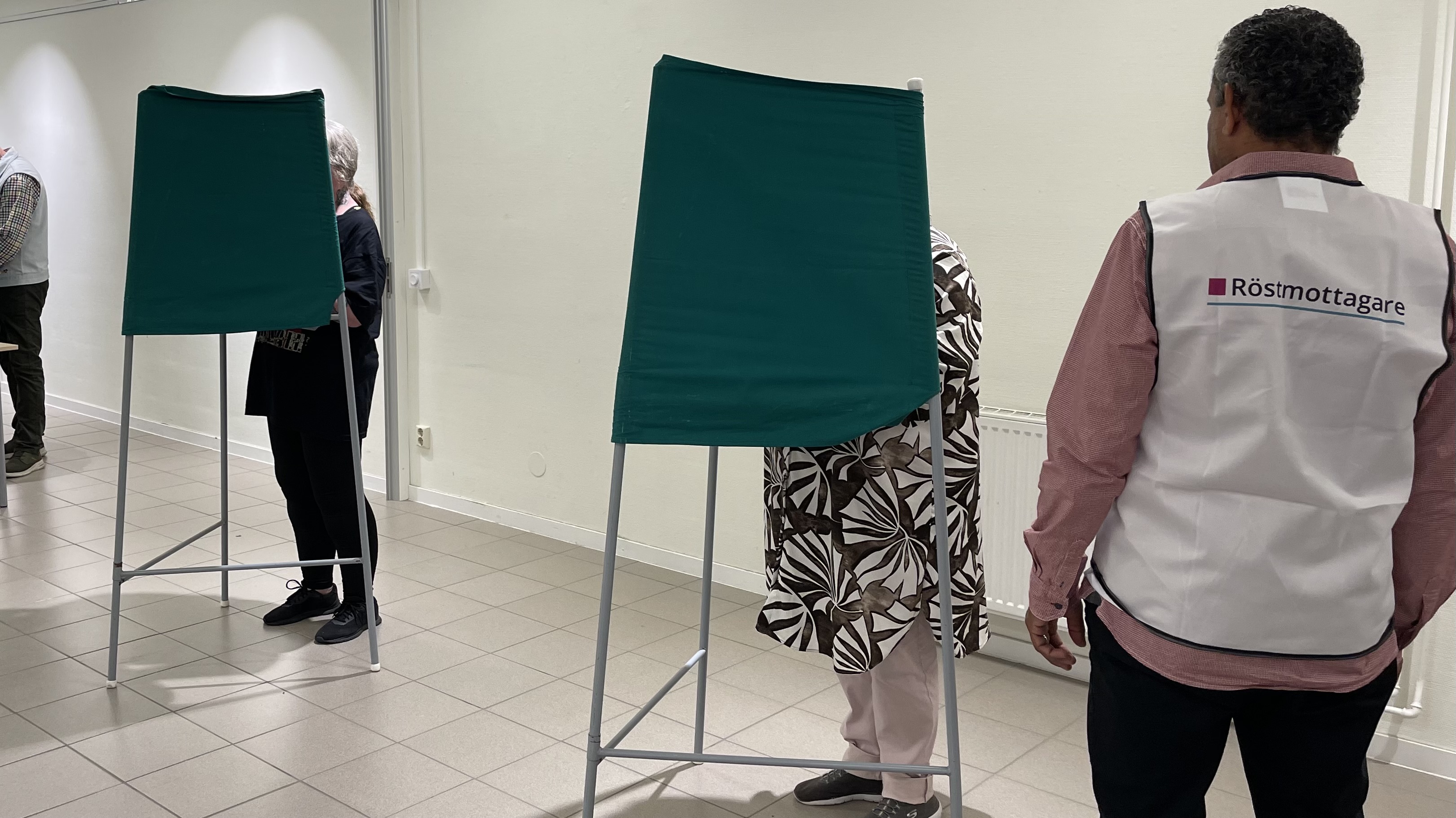 Vallokal. Personer i röstningsbås och röstmottagare