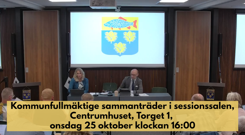 Kommunfullmäktige sammanträder i sessionssalen, Centrumhuset, onsdag 25 oktober 2023. Information står med mörk text på beige bakgrund över bilden där man ser kommunfullmäktiges presidie och kommunens vapen på skärmar bakom.