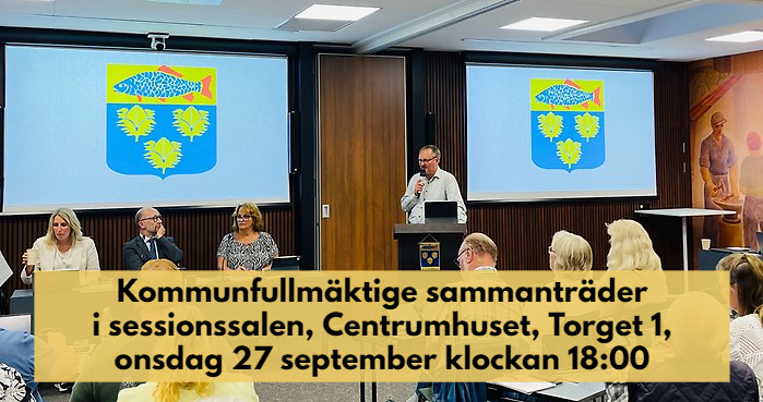 Kommunfullmäktige sammanträder i sessionssalen, Centrumhuset, onsdag 27 september 2023. Information står med mörk text på beige bakgrund över bilden där man ser kommunfullmäktiges presidie och kommunens vapen på skärmar bakom.