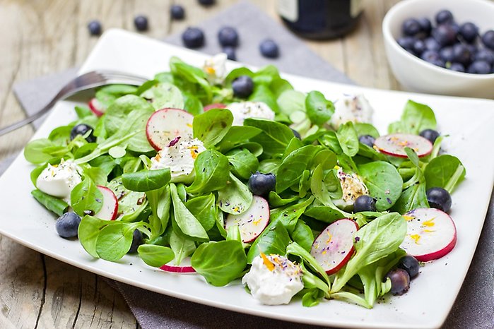Grönsaker, bland annat sallad och rädisor ligger på ett serveringsfat.