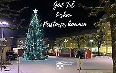 God Jul önskar Perstorps Kommun. Vintermotiv från torget med julgranen som lyser och snö på´marken.