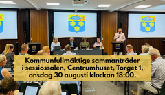 Kommunfullmäktige sammanträder i sessionssalen, Centrumhuset, onsdag 30 augusti 2023. Information står med mörk text på beige bakgrund över bilden där man ser kommunfullmäktiges presidie och kommunens vapen på skärmar bakom.