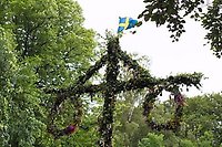 Bild på midsommarstång och grönskande träd i bakgrunden