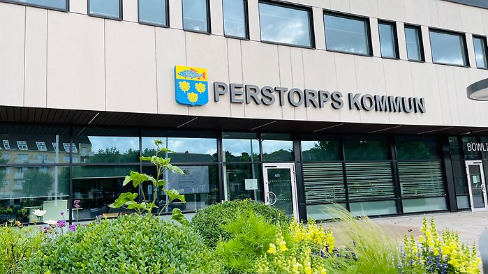 Bild som visar kommunhusets utsida, stor text där det står Perstorps kommun. Lite röna växter syns utanför.